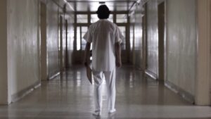 A doctor walking down a long, empty hospital hallway with a clipboard.