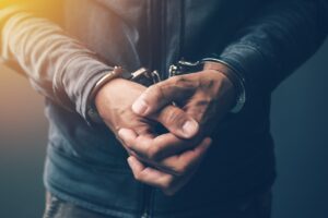 A close-up image of a person's hands in handcuffs, present Criminal Case Burden of Proof.